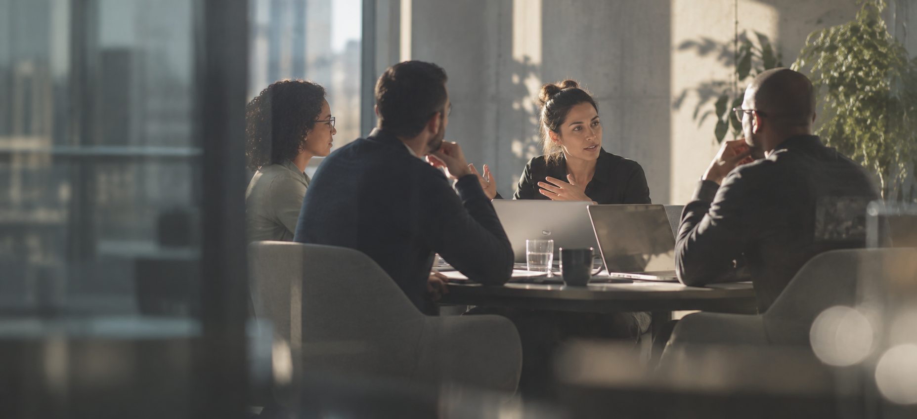 Four colleagues discussing ideas around a conference table in a sunlit modern office.